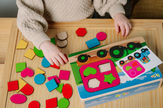 Child playing with colorful geometric shapes that are a part of a tractor puzzle.