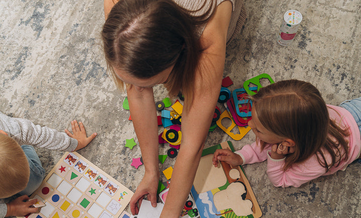 Woman and two children playing with colorful toys on a rug-covered floor.