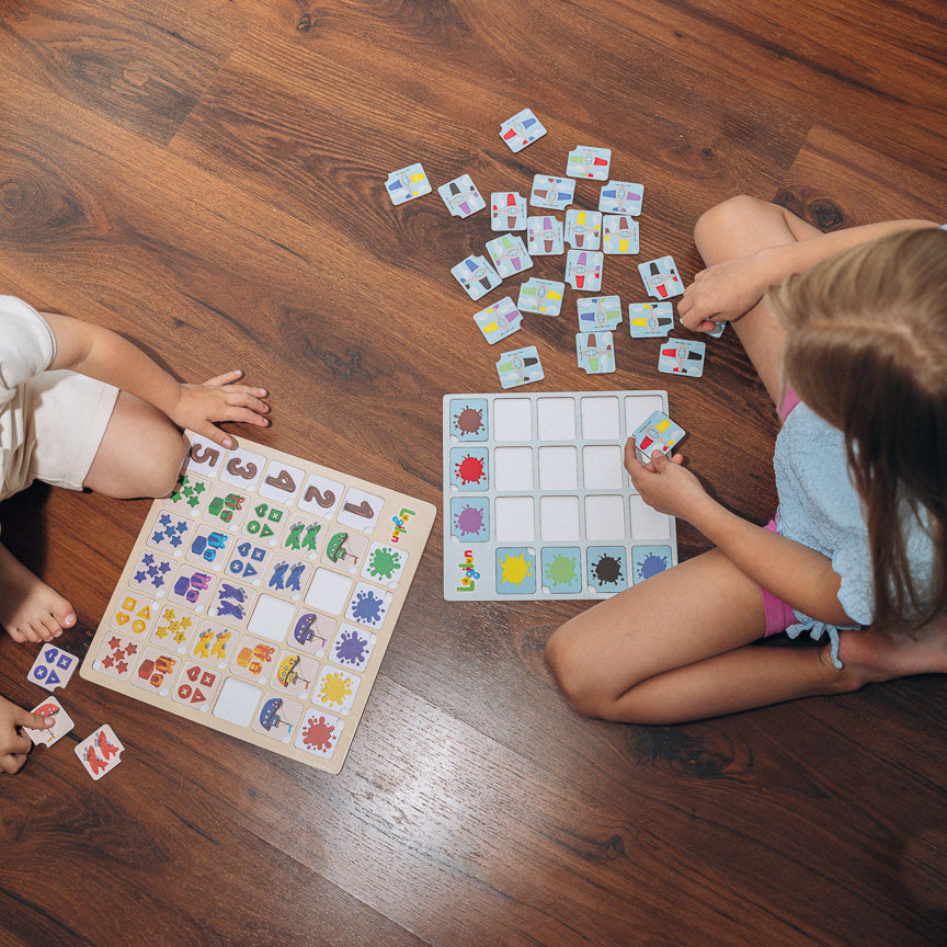 Two children playing with colorful game boards and cards on a wooden floor.